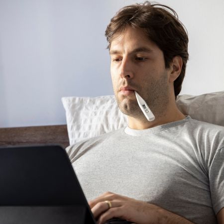 Man ziek bed laptop thermometer