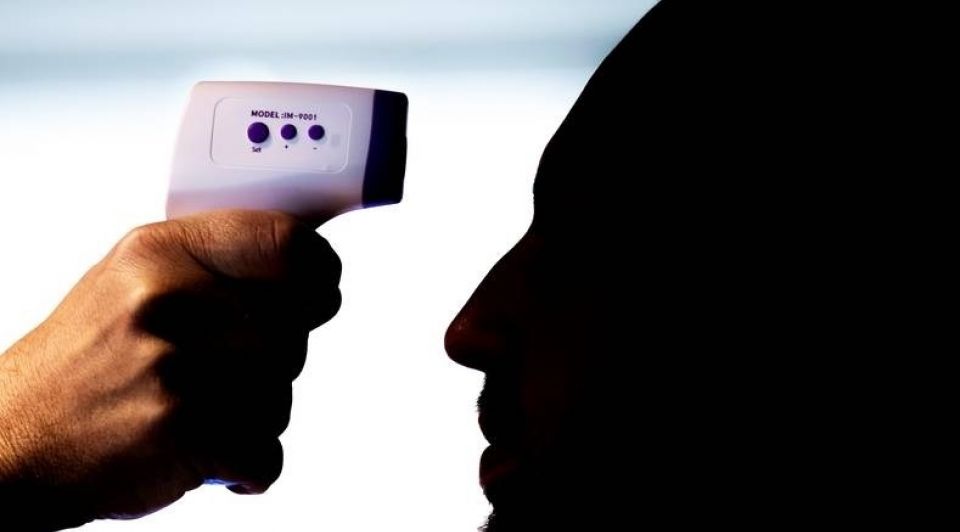 Een medewerker doet voor hoe de temperatuur wordt gemeten met een thermometer bij de ingang van het flexkantoor van Tribes op de Zuidas